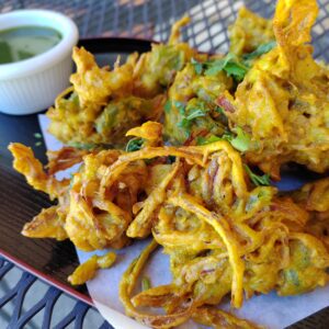 Mixed Vegetable Pakora Fritter originating from the Indian subcontinent, consists of vegetables such as potatoes and onions, coated in seasoned gram flour batter and deep fried. Served with Green Chutney